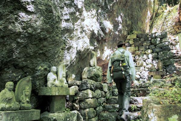 A guide walking next to a cave and small Buddhist staues.
